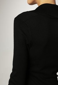 Pullover nero a maglia con colletto alto a costine, taglio aderente e texture liscia, con dettagli sulla cucitura della spalla e sul retro.