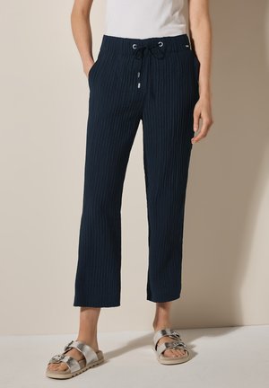 Pantaloni cropped rigati di colore blu navy con cintura elastica a cordoncino e tasche laterali, abbinati a sandali argentati con dettaglio a fibbia.
