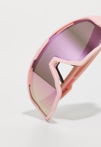 Ochelari de soare cu ramă din plastic roz, lentile violet cu gradient și design unghiular. Prezintă un mecanism de balama vizibil și un logo embosat.