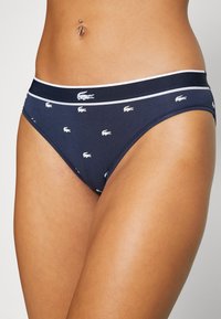 Tumši zila sieviešu apakšbikses ar elastīgu jostasvietu, kurai ir atkārtots balts logo raksts. Mīksta auduma ar gludu tekstūru.