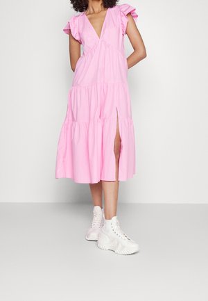 Robe en coton rose avec un design à étages, manches courtes à volants et une fente à l'avant. Assortie à des baskets blanches épaisses.