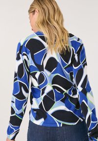 Lösa stickade tröja med ett livfullt abstrakt mönster i blått, vitt, svart och grönt. Stickad textur med långa ärmar och rund halsringning.