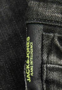 Tessuto in denim nero con una leggera texture, con un'etichetta verde che recita "JACK&JONES JEANS INTELLIGENCE" ben visibile.