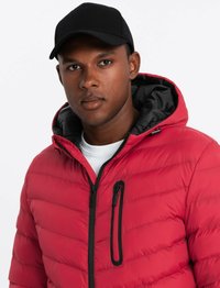 Veste en duvet rouge avec des coutures horizontales, des accents noirs et une poche poitrine zippée. Portée avec une casquette de baseball noire et un t-shirt blanc.