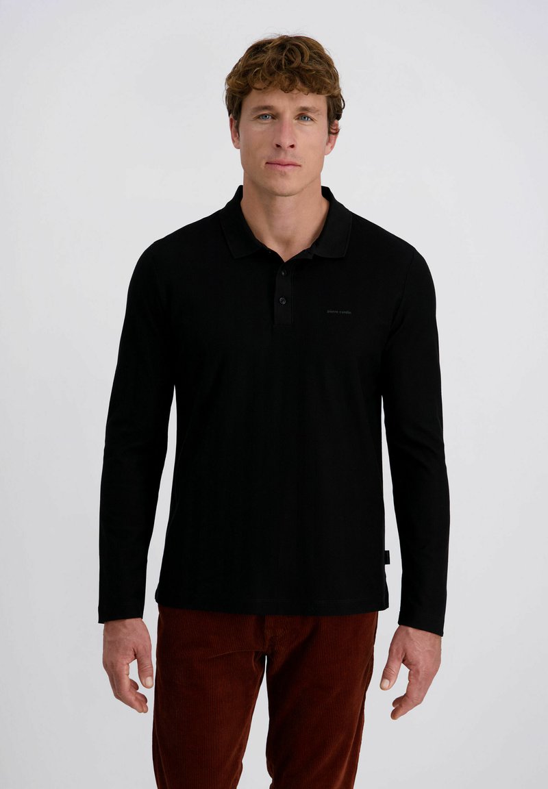 Zwart long-sleeve polo shirt gemaakt van zachte stof, met een kraag, knoopsluiting en een klein logo detail op de borst. Gepaard met bruine corduroy broeken.