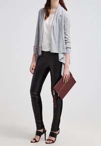 Grijze cardigan met franjes, witte top, zwarte neplederen broek en een bordeauxrode clutch. Zwarte sandalen met hakken maken de outfit compleet.