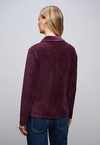 Lilla kordfløjlsskjorte med krave, lange ærmer og ribbet struktur. Bæres med blå jeans, som viser et glat rygdesign.