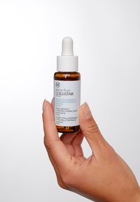 Brun glasdropperflaska med ett vitt lock och etikett, innehållande ett klart serum. Texten inkluderar "Hyaluronsyra + Polyglutaminsyra."