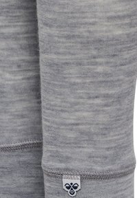 Ljusgrått tyg med ett texturerat stickmönster; har en vit etikett med en marinblå logotyp i fållen; sömlös sömnadsdetalj.