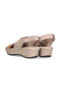 Sandalias de cuero beige con un pequeño tacón en cuña, que presentan un diseño recortado y detalles de costura a lo largo de la suela. Correa ajustable para un mejor ajuste.