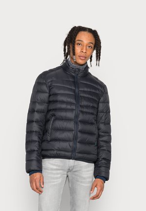 Marineblauer Pufferjacke mit Frontreißverschluss, hohem Kragen und horizontalem Steppmuster. Verfügt über zwei Seitentaschen und kontrastierende blaue Reißverschlusselemente.