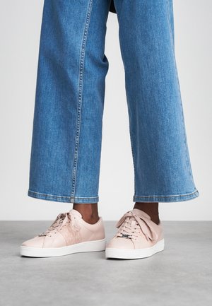 Baskets roses claires avec une finition en cuir lisse, des panneaux latéraux à motifs et des lacets épais, associées à un pantalon cropped en denim bleu large.