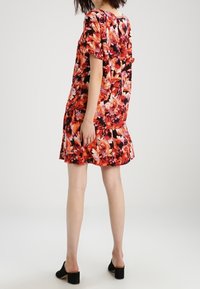 Robe florale avec des motifs vibrants de rouge, orange et rose, à manches courtes et à coupe décontractée. La vue de dos met en avant des détails de plis et un ourlet.