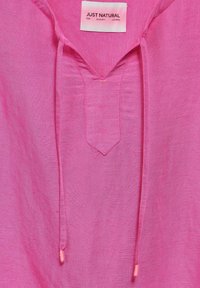 Rosa linneskjorta med V-ringning och sprund; har två dragsko med rosa spetsar. Etiketten säger "JUST NATURAL." Slät textur.