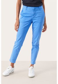 Light blue, slim-fit trousers with a flat front, belt loops, and ankle length, made from smooth fabric. Worn with white sneakers.