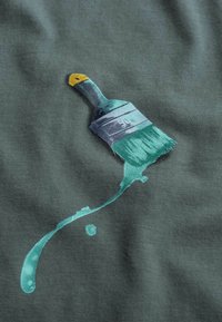 Groene stof met een geschilderde kwast met een gele handvat en turquoise haren, met verfsproeien eronder.