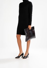 Svart stickad klänning med hög krage, matchad med en glänsande svart clutch med ormskinnsmönster och svarta klackar med metallisk accent.