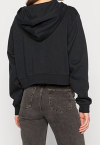 Zwarte cropped hoodie met capuchon en trekkoord, geribbelde manchetten en zoom, gecombineerd met donkergrijze high-waisted jeans met achterzakken.