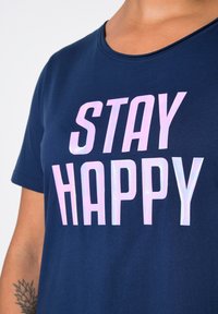 Námořnické tričko z měkké bavlny s kulatým výstřihem, na kterém jsou velké růžové iridescentní nápisy "STAY HAPPY". Krátké rukávy, hladká textura.