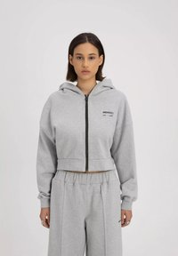 Grijze cropped hoodie met een frontale rits en een capuchon met trekkoord. Bevat een gedrukt logo op de borst en heeft een relaxte pasvorm. Gecombineerd met bijpassende grijze broek.