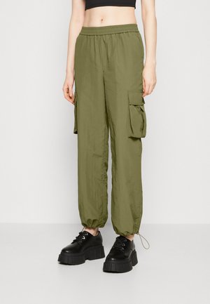 Cargo pants in olive green fabric with an elastic waistband and ankle cuffs. Features side pockets for utility. Paired with black platform shoes.