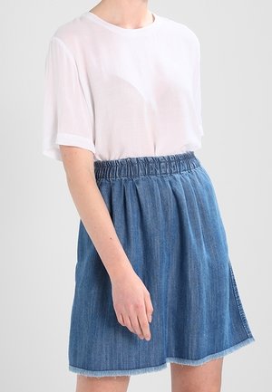 Biała, luźna bluzka z krótkim rękawem zestawiona z niebieską spódnicą dżinsową z elastycznym pasem, zakładkami i postrzępionym dołem.