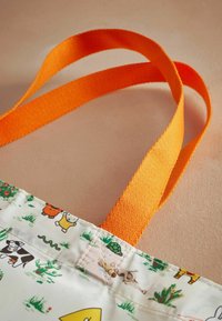 Reusable bag with a white, patterned fabric featuring animals and plants, complemented by bright orange flat straps.