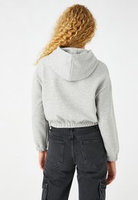Sudadera gris corta con capucha, dobladillo y puños elásticos; combinada con pantalones cargo negros de tiro alto que cuentan con bolsillos y un diseño ajustado.