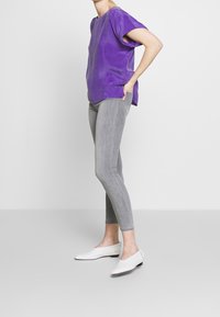 Lila oversized t-shirt med korta ärmar, tillsammans med grå skinny jeans och vita slip-on skor. Enkelt, avslappnat mönster med minimal detaljering.