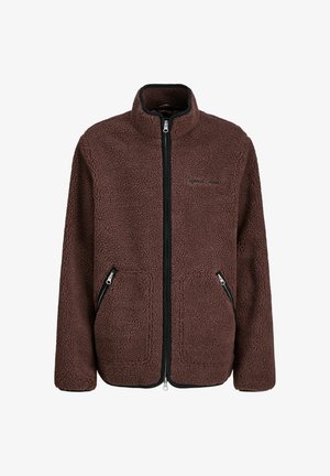 Brązowa polarowa kurtka z wysokim kołnierzem, zamykanymi na zamek kieszeniami i luźnym krojem, noszona na koszuli w kratę oraz dopasowana do luźnych niebieskich dżinsów.