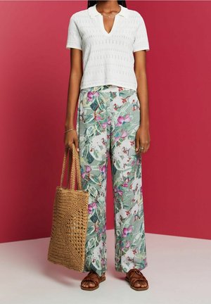 Haut blanc à manches courtes avec col en V, associé à un pantalon large à fleurs vertes et roses. Comprend un sac fourre-tout tressé beige et des sandales marron.