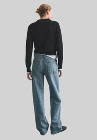 Pullover nero, jeans a gamba larga blu chiaro e scarpe nere. I jeans hanno tasche posteriori; il pullover ha un collo rotondo e un orlo a coste.