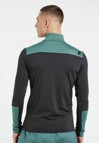 Langärmliges Sportoberteil in Schwarz und Petrol. Das Oberteil verfügt über einen hohen Kragen, kontrastierende Schulterpanels und ein Logo auf dem Rücken.