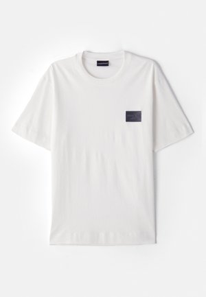 Valkoinen lyhythihainen puuvillainen t-paita pyöreällä pääntiellä ja vasemman rinnan kohdalla pienellä mustalla suorakulmaisella logopainatuksella.