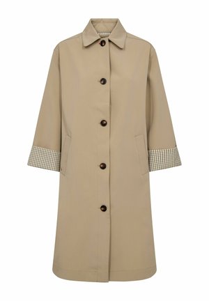Béžový dlhý kabát s klasickým golierom, čiernymi gombíkmi po celej prednej časti, bočnými vreckami a vzorovanými vnútornými manžetami rukávov viditeľnými na prehnutých rukávoch.