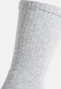 Grau gerippte Socke mit weicher Textur, ausgestattet mit einem verstärkten Bündchen und einer glatten Oberfläche, teilweise vor einem weißen Hintergrund gezeigt.