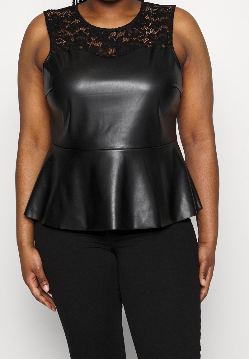 Femme portant un haut peplum sans manches en similicuir noir avec un détail en dentelle sur le haut de la poitrine et des épaules, associé à un pantalon noir.