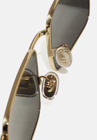 Lunettes de soleil en métal doré avec des verres gris foncé légèrement arrondis. Dispose de plaquettes de nez transparentes avec "RSF" gravé et d'un design de monture épuré.