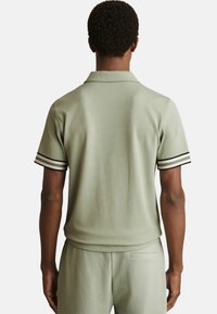 Tricou polo scurt cu mâneci scurte, de culoare verde deschis, confecționat dintr-un material texturat, cu accente în dungi alb-negru pe mâneci și un design clasic al gulerului.