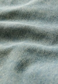 Ljusblå denimtyg med en texturerad yta, som har subtila diagonala vävmönster och mjuka, naturliga veck.