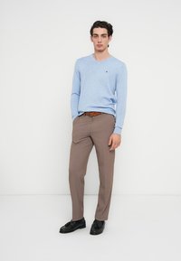 Γαλάζιο πουλόβερ με V λαιμόκοψη, μπεζ παντελόνι, μαύρα παπούτσια, καφέ ζώνη. Το πουλόβερ έχει μικρό λογότυπο στο στήθος, με απαλή υφή.