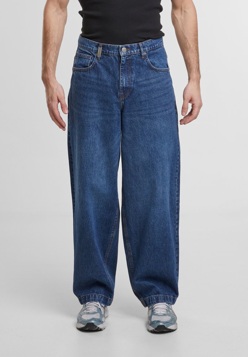 Jean en denim bleu ample avec une fermeture éclair, de grandes poches avant et des ourlets retroussés. Fabriqué en denim de coton texturé et doux.