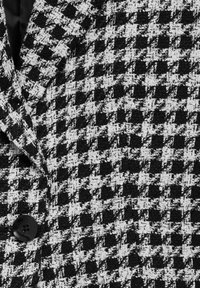 Tissu à motif pied-de-poule noir et blanc avec un bouton noir visible et une partie d'un col à revers.