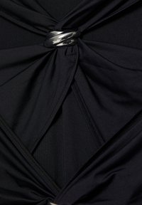 Zwarte stof samengebonden en gedraaid door een glanzende zilveren metalen ring, wat resulteert in een geplooid en gelaagd textielontwerp.