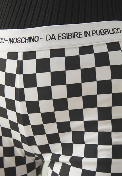 Juoda ir balta languota legingo kelnės su elastine juosta, ant kurios juodu raštu yra užrašas "Moschino - da esibire in pubblico". Sklandi tekstūra.