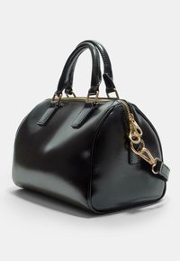 Sac à main en cuir brillant noir avec une forme ronde, deux poignées supérieures, des accessoires en métal doré, une fermeture éclair et une bandoulière détachable.