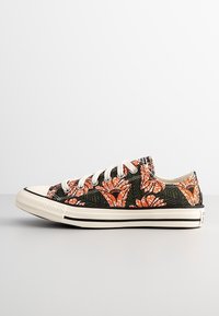 Baskets en toile sur fond noir avec des motifs floraux orange. Lacets blancs et semelle en caoutchouc, avec accent de rayure noire.