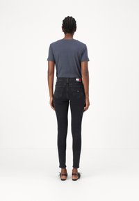 Fekete slim fit farmernadrág magas derekkal, hátsó zsebekkel és márkázott derékkal. Szürke, rövid ujjú pólóval és fekete cipővel párosítva.