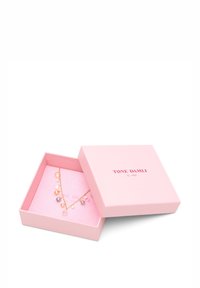 Gold necklace with multi-colored gemstone accents, displayed on soft pink fabric inside a light pink box with "TONE DAMILI" branding.
