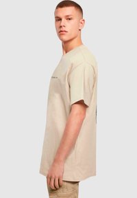 Bežinė medvilninė t-shirt su trumpomis rankovėmis, turinti apvalų kaklą ir grafišką spaudą krūtinėje. Tiesus siluetas ir laisvas kirpimas.
